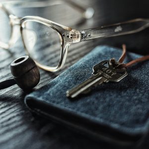 A detailed image of glasses, a key, and a pipe on a textured wooden table.