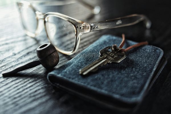 A detailed image of glasses, a key, and a pipe on a textured wooden table.