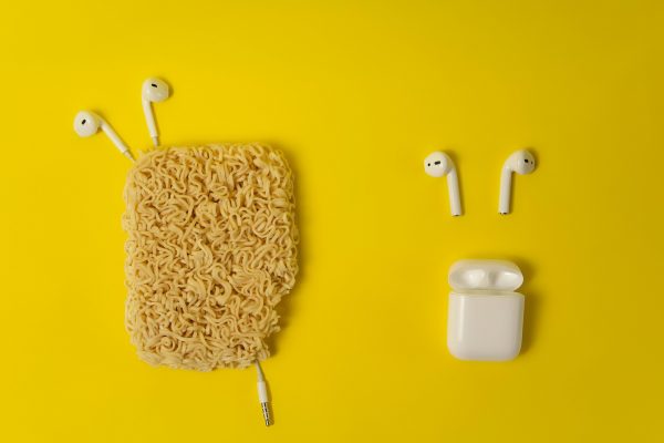 Unique composition with earbuds and noodles on a vibrant yellow background, showcasing modern technology and creativity.