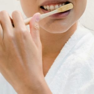 A person brushing their teeth with an eco-friendly bamboo toothbrush, promoting oral hygiene.